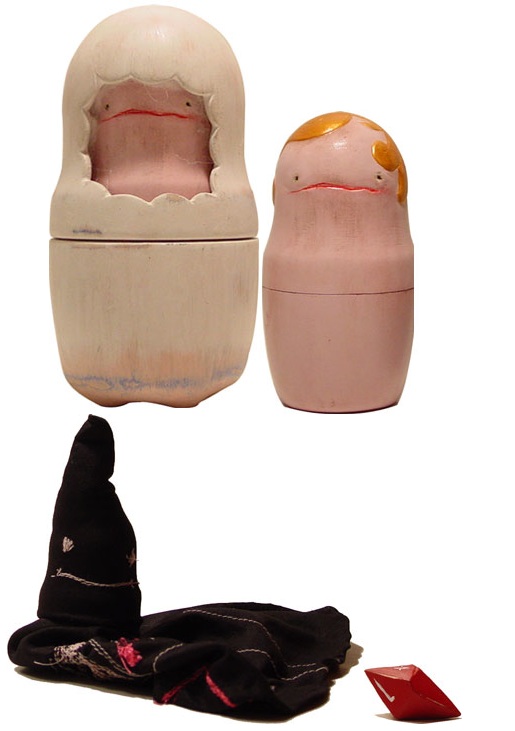 Two hand-painted matryoshka-style dolls with sad pink faces — one hooded in cream, one with a golden bob — above a black pointed hood and a tiny red gem